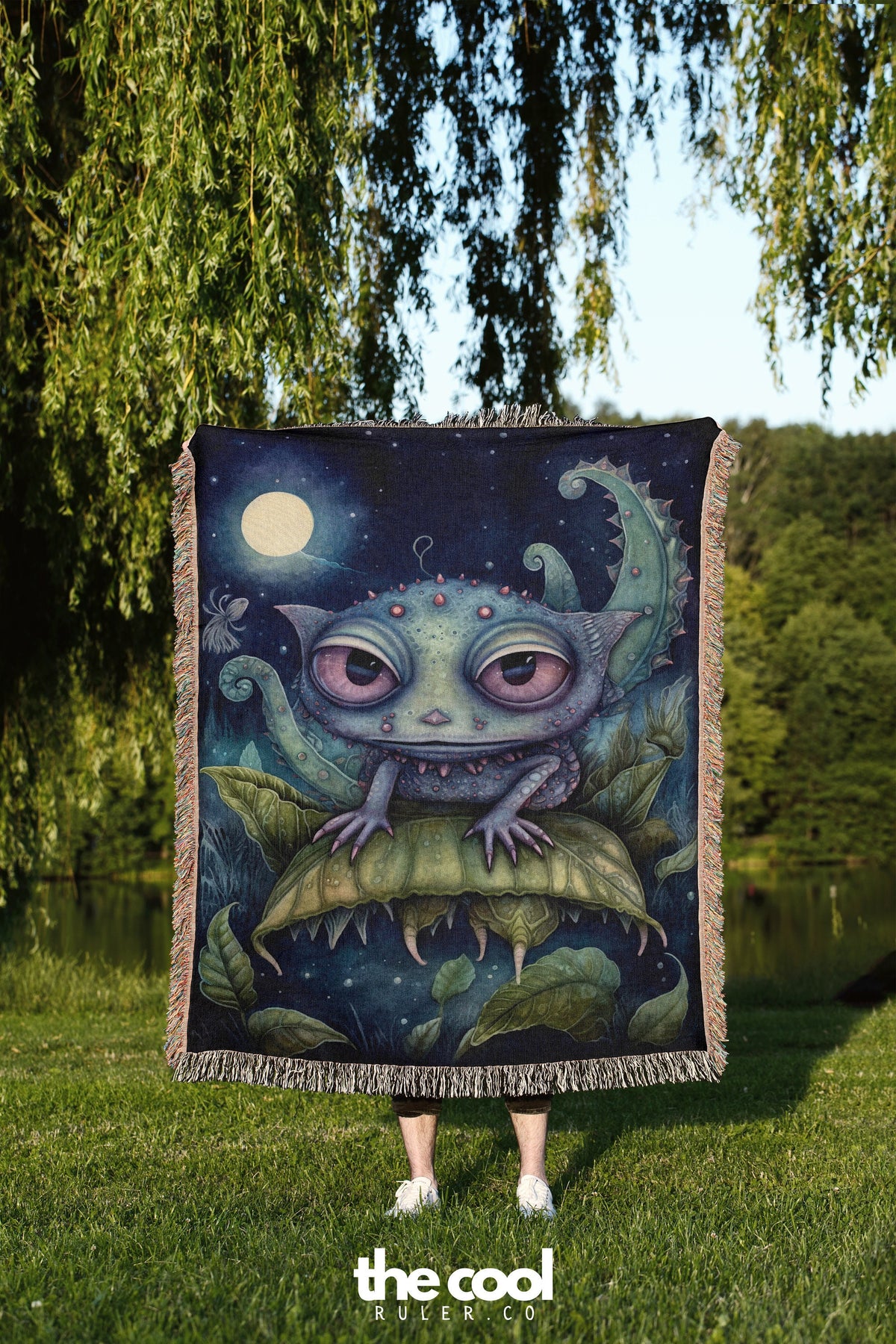 a woman standing in the grass holding a blanket with an image of a creature on