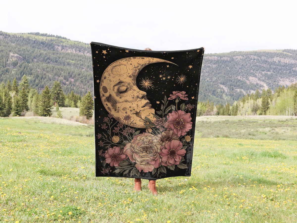 a woman standing in a field holding a blanket with a moon and flowers on it