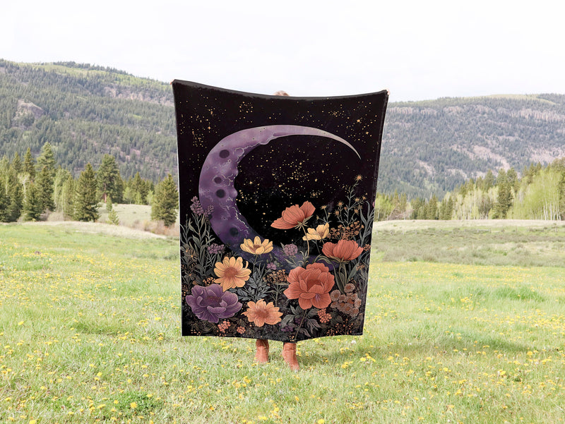 a woman holding a black and purple blanket with a moon and flowers on it