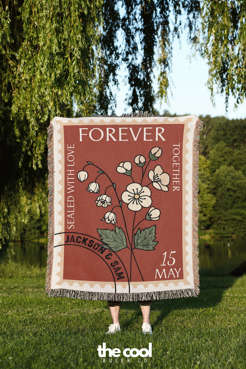 a woman standing in the grass holding a blanket with flowers on it