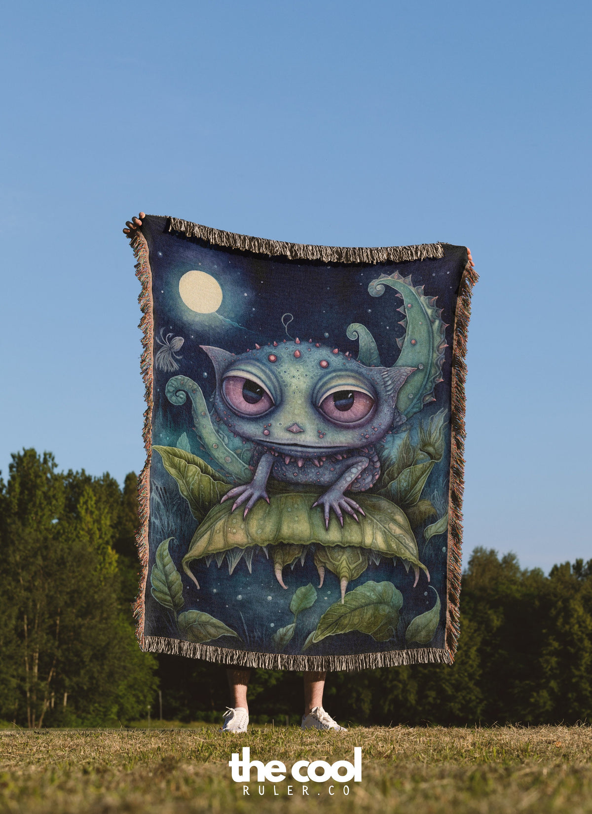 a woman standing in a field holding a blanket with an image of a creature on