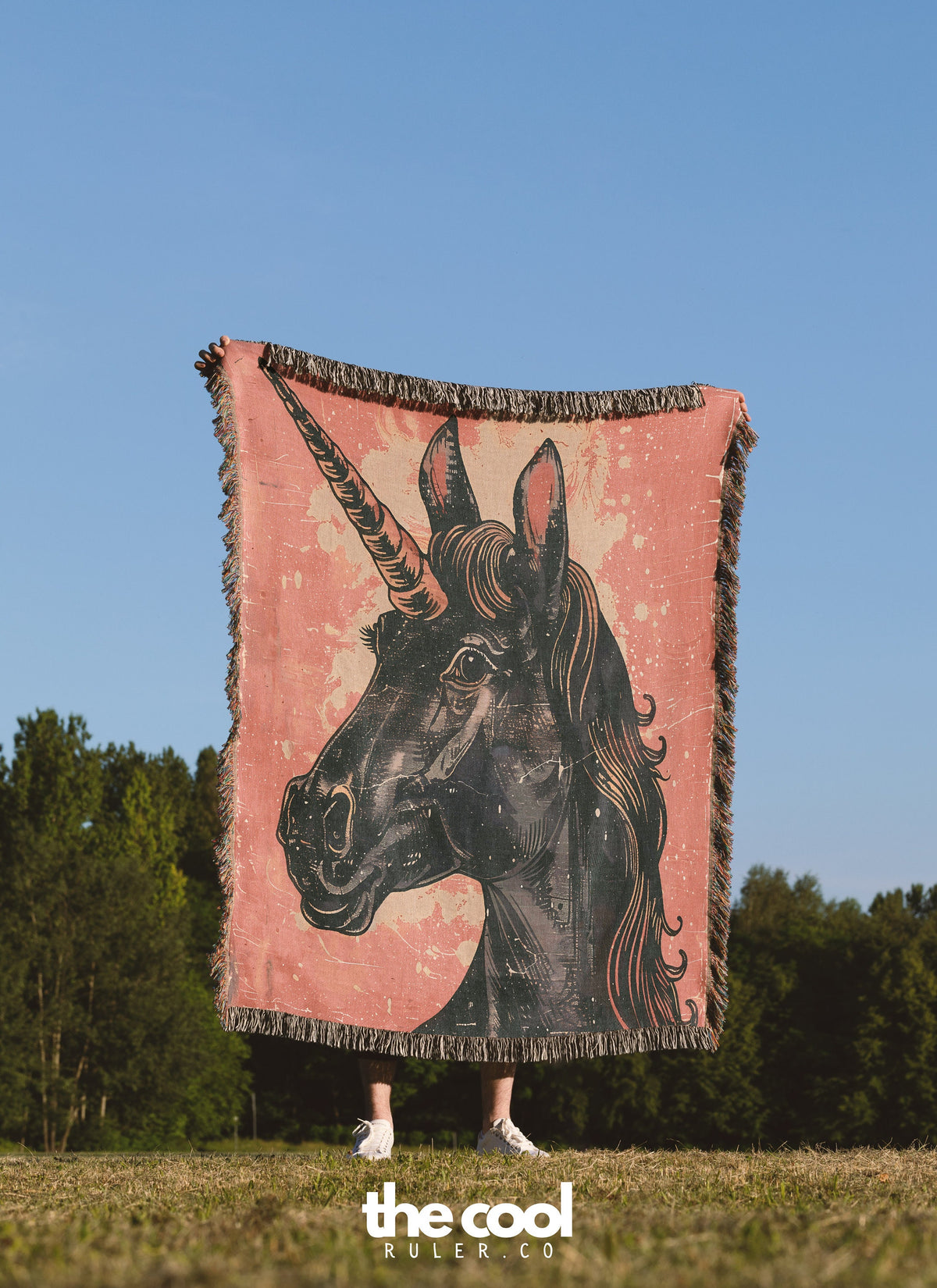 a woman standing in a field holding a blanket with a picture of a unicorn on